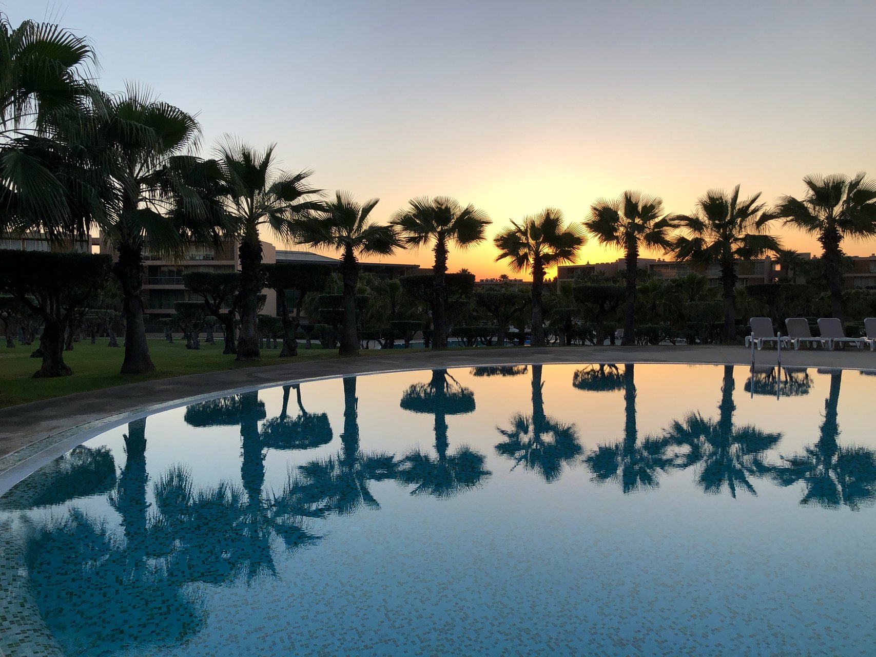 Luxury T3 Apartment view of the sunset in the pool, at Salgados Vila das Lagoas, with palm tree reflections, Albufeira, Portugal.