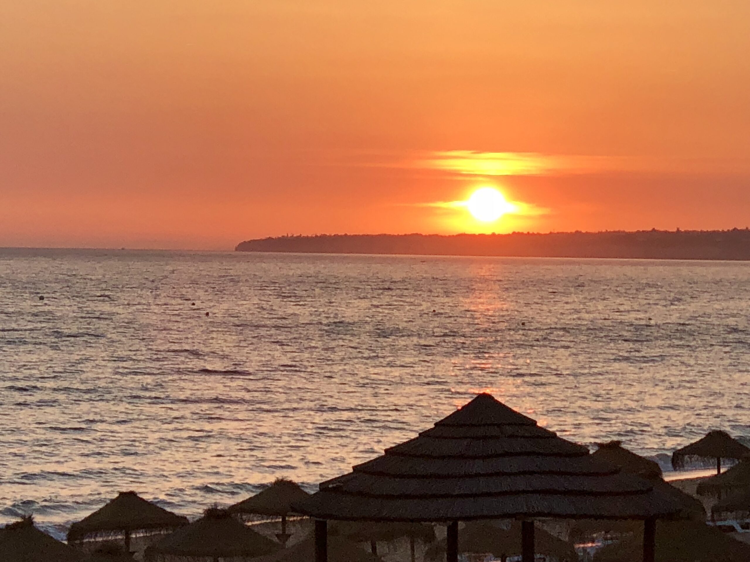 Pôr do sol na Praia dos Salgados, Albufeira, com guarda-sóis e mar tranquilo