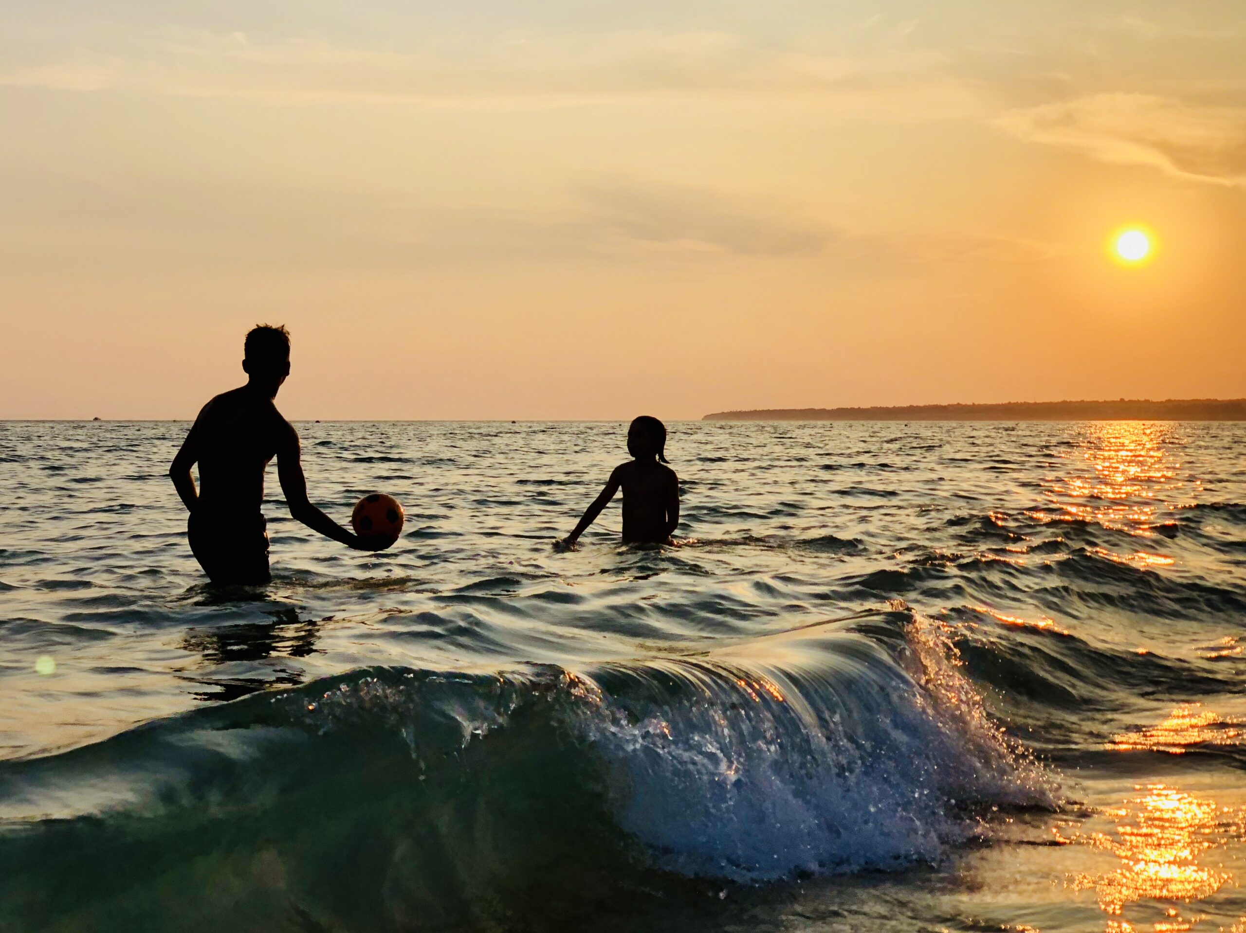 Crianças a jogar à bola no mar durante pôr do sol na Praia dos Salgados, Albufeira.