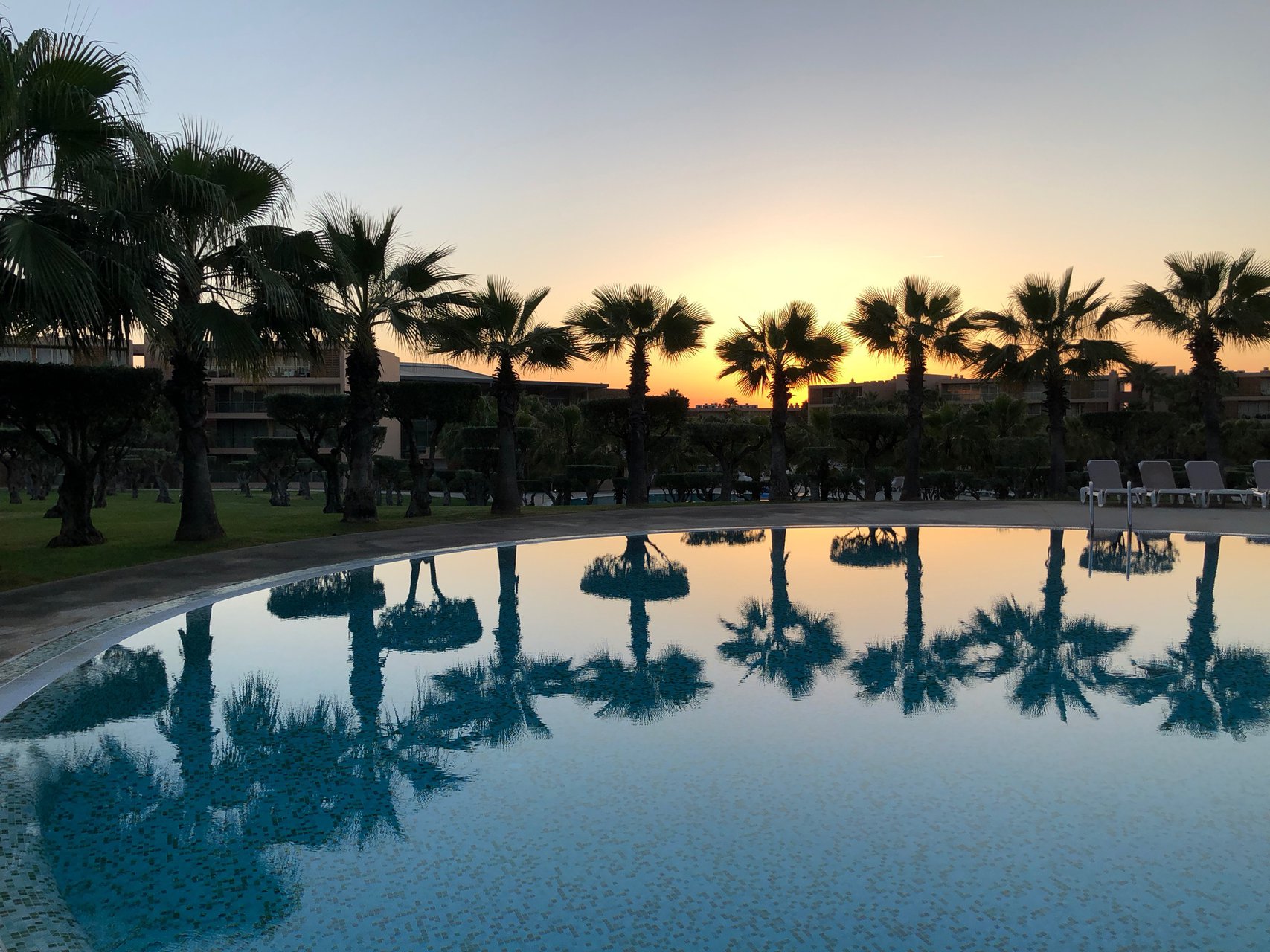 Entardecer tranquilo com reflexo de palmeiras na piscina na Vila das Lagoas, Salgados